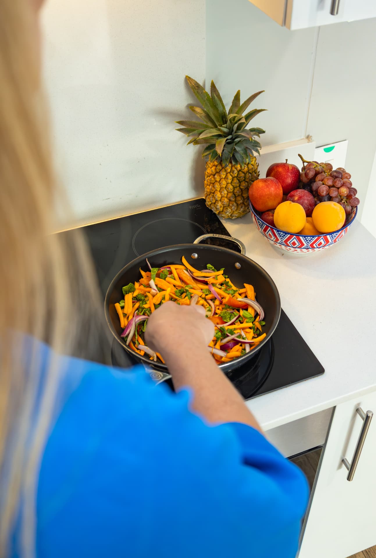 Dietitian preparing a colourful vegetable dish beside a bowl of fresh fruit